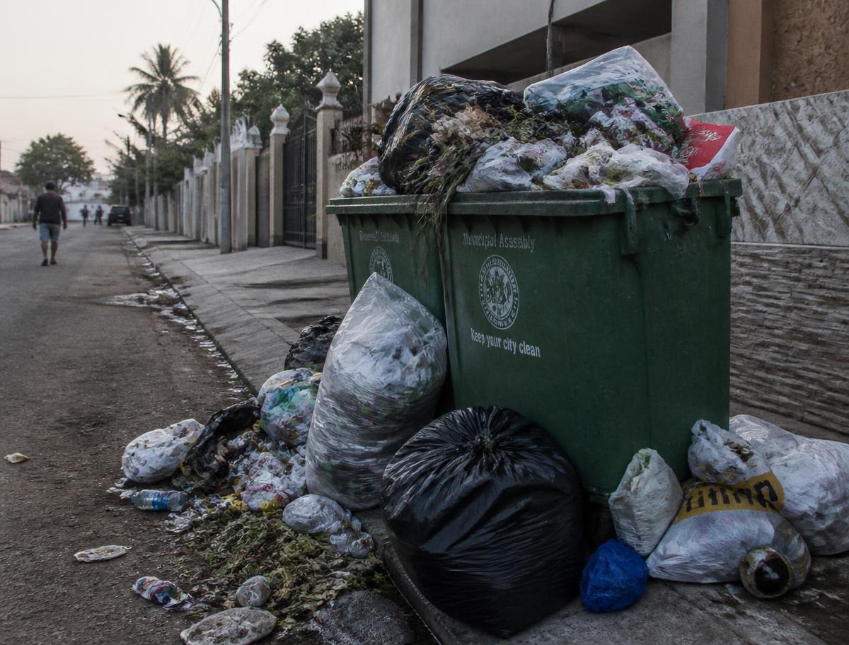 Overflowing municipal bins spilling refuse onto a residential pavement